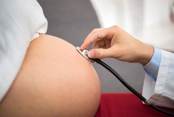 Accouchement sur le cote : image d'un medecin oscultant le ventre d'une femme enceinte a l'aide d'un stetoscope