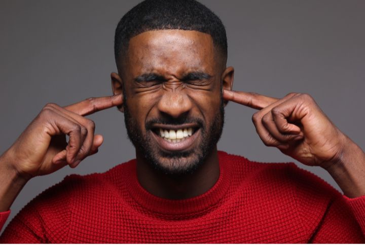 Hyperacusie : un homme se bouche les oreilles avec ses doigts et grimace de douleur.
