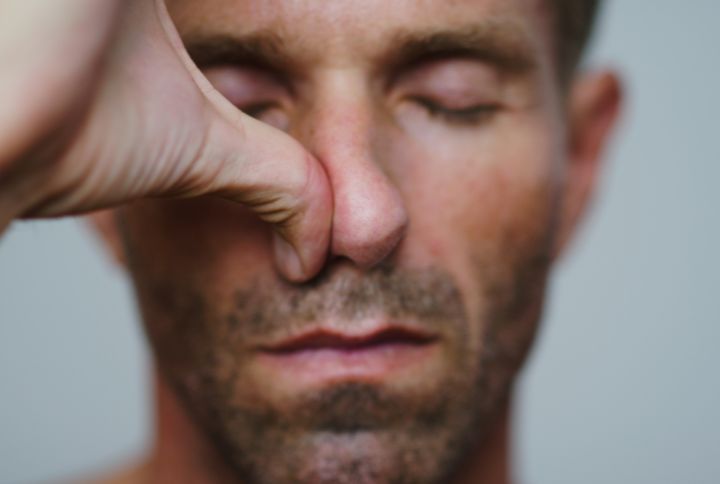 Polypes nasaux. Gros plan sur le visage d'un homme qui ferme les yeux et appuie fortement sur une de ses narines avec son pouce.