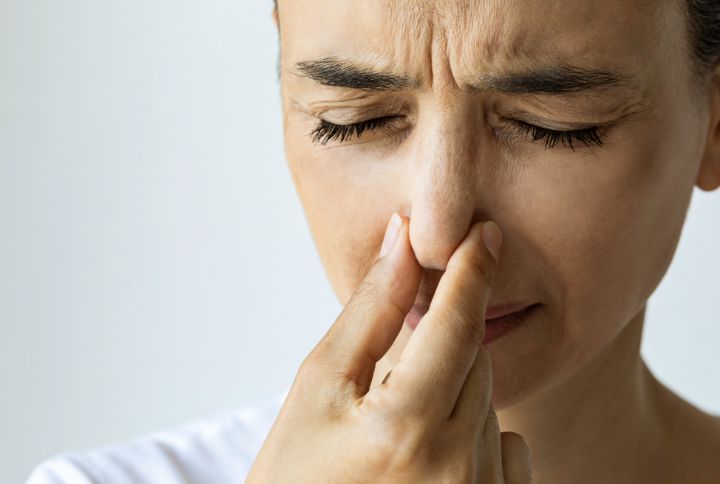 Hyposmie : gros plan sur le visage d'une femme, visiblement gênée, qui se bouche les narines et ferme les yeux.