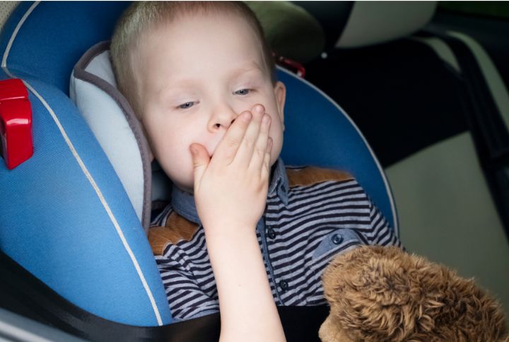 Mal des transports, comment l’éviter et le soigner ? Un jeune enfant dans son siège à l'arrière d'une voiture, met sa main devant la bouche et a le teint blême.
