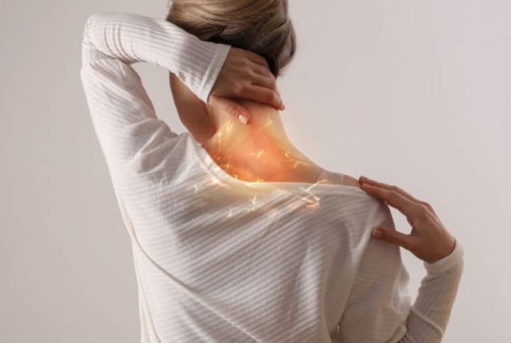 Névralgie cervico-brachiale : durée traitement symptôme : une femme vue de dos se touche la nuque et l'épaule. La douleur ressentie est figurée par une lumière sur son cou.